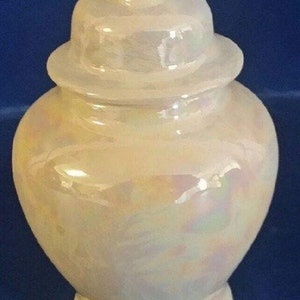 May include: A white ceramic jar with a lid. The jar has a pearlescent finish with iridescent swirls. The lid is round and has a smooth surface.