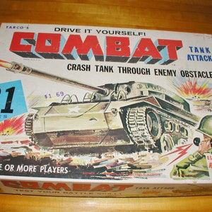 May include: A vintage box for a Combat Tank Attack game. The box features a green, brown, and gray tank with a white star on the side. The box is labeled "Drive It Yourself! Combat Tank Attack" and "Crash Tank Through Enemy Obstacles". The box also includes a picture of a soldier with an electronic remote control.