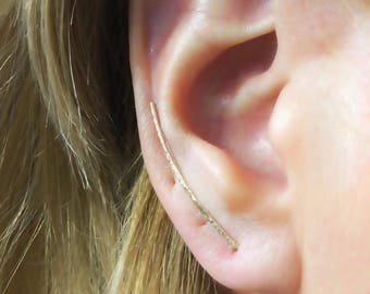 Puede incluir: Un pendiente de aro de oro con acabado texturizado. El aro es curvo y se extiende desde la parte superior de la oreja hasta el lóbulo.