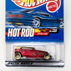 May include: A red Hot Wheels die-cast toy car with gold wheels and flames painted on the side. The car is labeled "Hot Rod Magazine Phaeton 1 of 4 Cars".