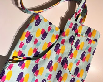 May include: A light blue tote bag with a pattern of colorful ghosts. The bag has a single strap and a large pocket on the front.