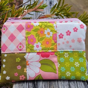 May include: A patchwork zipped pouch featuring floral and geometric patterns in pink, green, and white. The pouch has a pink zip and a leather pull tab. The design is handmade, with a floral theme.