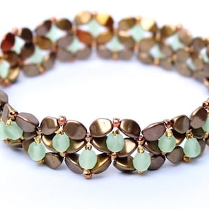 Könnte beinhalten: Ein braunes und grünes Perlenarmband mit einem gewebten Muster. Das Armband besteht aus kleinen, ovalen Perlen und runden Perlen.