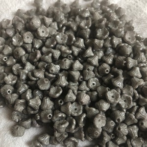 Könnte beinhalten: Ein großer Haufen grauer Glasperlen in Blütenform. Die Perlen haben eine strukturierte Oberfläche und sind perfekt für die Schmuckherstellung.