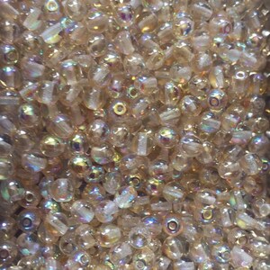 May include: A large quantity of iridescent glass beads in a light brown colour. The beads are round and have a smooth, shiny finish.