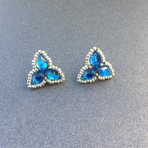 May include: A pair of silver earrings with blue glass beads in a triangular shape.
