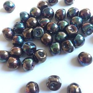 Könnte beinhalten: Ein Haufen irisierender dunkelbrauner Glasperlen. Die Perlen haben eine leicht quadratische Form und ein Loch in der Mitte.