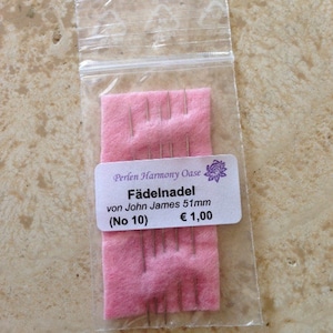 May include: A pack of 5 silver beading needles, labelled "Fädelnadel von John James 51mm (No 10) € 1,00" on a pink background.