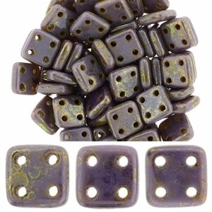 Puede incluir: Un montón de cuentas cuadradas de vidrio de color morado y dorado con cuatro agujeros cada una. Las cuentas tienen un aspecto moteado y jaspeado.