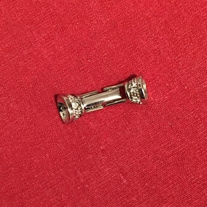 Puede incluir: Un cierre de pulsera plateado con una fila de piedras de cristal transparentes en cada extremo.