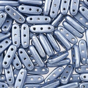 May include: A close-up of a pile of light blue glass beads. The beads are oval shaped and have four holes in them.