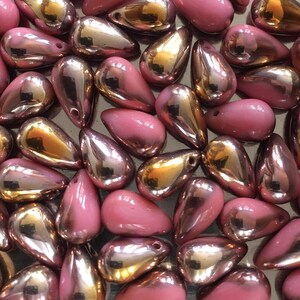May include: A collection of teardrop-shaped glass beads in shades of pink and gold. The beads have a glossy, iridescent finish.
