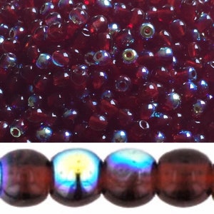 Könnte beinhalten: Nahaufnahme eines Haufens kleiner, dunkelroter Glasperlen mit irisierendem Schimmer. Die Perlen sind rund und haben eine leicht tropfenförmige Form. Unter den Perlen befindet sich eine Reihe größerer, runder, dunkelroter Glasperlen mit irisierendem Schimmer. Die Perlen haben ein Muster eines Sonnenuntergangs.