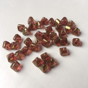 May include: A group of small, iridescent, red and gold, pyramid-shaped glass beads.
