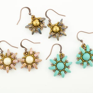 Könnte beinhalten: Vier Paar Perlenohrringe mit einem Sternburst-Design. Zwei Paare haben ein hellrosa und goldenes Farbschema mit einem weißen Perlenmittelpunkt. Die anderen beiden Paare haben ein türkisfarbenes und goldenes Farbschema mit einem türkisfarbenen Mittelpunkt.