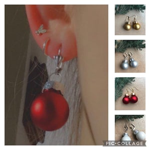Puede incluir: Un par de pendientes con pequeños adornos redondos que se asemejan a bolas de Navidad. Las bolas están disponibles en dorado, plateado, rojo y blanco.