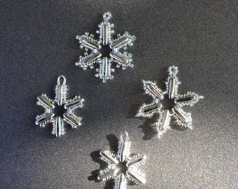 May include: Four silver snowflake ornaments of varying sizes on a gray background.