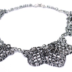 May include: A silver and black beaded necklace with a delicate, intricate design. The necklace features four large, leaf-shaped pendants.