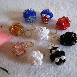 Könnte beinhalten: Acht Perlenornamente mit goldenen Schlaufen. Die Ornamente sind in verschiedenen Farben, darunter Rot, Weiß, Schwarz, Blau und Pink.