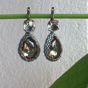 May include: A pair of dangle earrings with a teardrop-shaped crystal accented with gold and blue beads. The earrings have a silver-toned hook closure.
