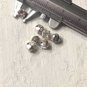 May include: Close-up of six silver-toned metal embellishments with clear rhinestones. The embellishments are approximately 1.2 cm in diameter. A ruler is in the background.