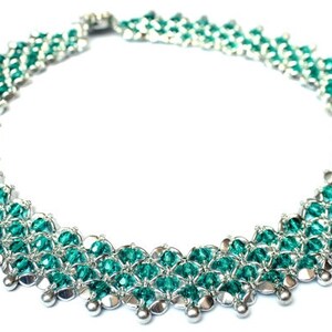 Puede incluir: Un collar de cuentas plateadas y verde turquesa con un diseño delicado e intrincado. El collar está hecho de pequeñas cuentas redondas que están dispuestas en un patrón de círculos superpuestos.