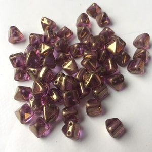 May include: A pile of small, iridescent purple and gold triangle-shaped beads.