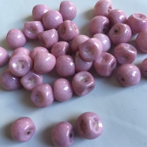Può includere: Una collezione di perline di vetro rosa pallido, ciascuna con una forma leggermente irregolare e una finitura liscia e lucida.