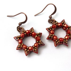 Könnte beinhalten: Ein Paar rote und goldene sternförmige Ohrringe mit einem Perlenmuster.