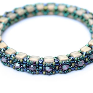 May include: A beaded bracelet featuring a multi-coloured design. The bracelet is crafted with small, square-shaped beads in shades of beige, green, and blue. The beads are arranged in a repeating pattern, creating a geometric design.