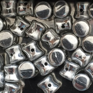 Peut inclure: Gros plan sur une collection de perles en verre de couleur argent. Les perles sont de formes variées, notamment rondes, carrées et en forme de larme. Les perles sont brillantes et réfléchissantes.