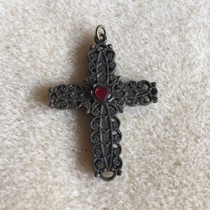 Può includere: Un ciondolo a forma di croce in filigrana con un gioiello rosso al centro.