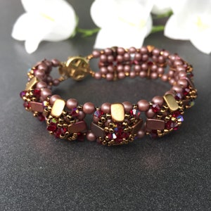 May include: A beaded bracelet in a gold and brown colour scheme. The bracelet features a repeating pattern of square-shaped beads and smaller, round beads. The bracelet is made with a variety of different beads, including some that have a metallic finish.
