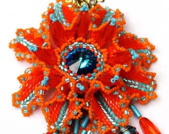 May include: A beaded necklace with a large orange and turquoise flower pendant. The pendant features a large blue crystal in the center. The necklace is made of small beads and has a gold clasp.