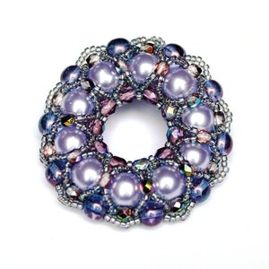 Puede incluir: Un anillo circular de cuentas moradas y plateadas. El anillo está hecho de cuentas pequeñas y perlas.