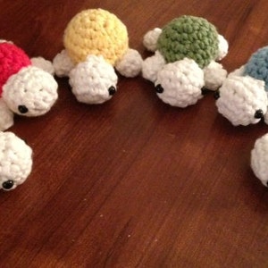 May include: Seven crocheted turtle toys in different colors, including orange, red, yellow, green, blue, and purple. Each turtle has a white shell and black eyes.