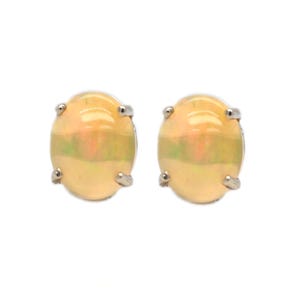 Könnte beinhalten: Ein Paar oval geformte Ohrstecker mit glatten, durchscheinenden Cabochon-Opalen, die irisierende Farbreflexe aufweisen. Jeder Opal ist in einer schlichten, silberfarbenen Metallfassung mit vier Krappen sicher gefasst und wirkt poliert.