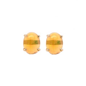 Könnte beinhalten: Ein Paar ovaler Ohrstecker mit glatten, durchscheinenden orange-gelben Cabochon-Steinen, die in goldfarbenen Metallfassungen sitzen. Die Steine haben ein weiches, leuchtendes Aussehen mit subtilen internen Farbvariationen und einer glatten Oberfläche.