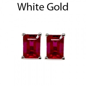 Könnte beinhalten: Ein Paar Ohrstecker mit rechteckigen, im Smaragdschliff geschliffenen roten Edelsteinen in Weißgoldfassung. Der Text White Gold steht über den Ohrringen. Jeder Edelstein wird von vier kleinen Metallkrampen an den Ecken gehalten.
