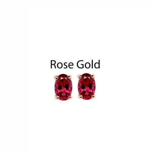 May include: Rose gold stud earrings with oval-cut, deep red gemstones. The earrings are set in a rose gold metal and are displayed on a white background. The text "Rose Gold" is above the earrings.