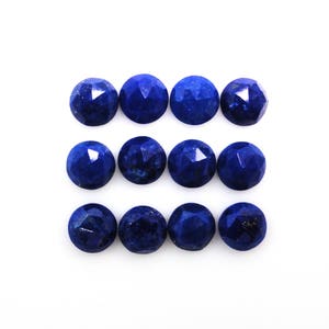Può includere: Dodici perline di pietra preziosa sfaccettate di colore blu scuro, disposte in tre file di quattro perline ciascuna, su uno sfondo bianco.