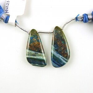 May include: Two teardrop-shaped green, blue, and brown gemstone beads with white streaks. The beads are strung on a silver wire.