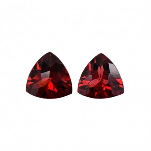May include: Two triangular red gemstones with a faceted cut.