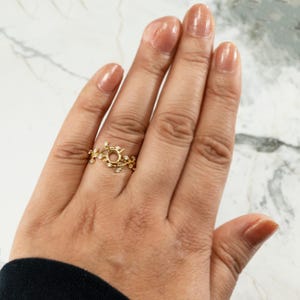 Puede incluir: Un anillo de oro con un delicado dise&ntilde;o de vid y peque&ntilde;as piedras transparentes. El anillo est&aacute; en el dedo de una persona.