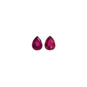 May include: Two pear-shaped, faceted rubies with a deep red color. The gemstones are displayed against a white background, showcasing their clarity and brilliance. Ideal for jewelry making or gemstone collection.