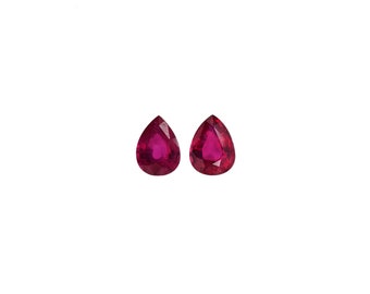 May include: Two pear-shaped, faceted rubies with a deep red color. The gemstones are displayed against a white background, showcasing their clarity and brilliance. Ideal for jewelry making or gemstone collection.