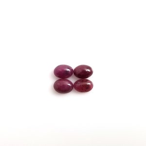 May include: Four oval-shaped, deep pink gemstones. The gemstones are smooth and polished.