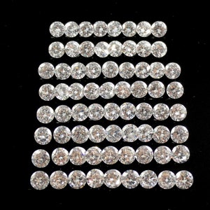 May include: A collection of round, clear, faceted gemstones arranged in rows on a black background. The gemstones are likely diamonds or cubic zirconia.