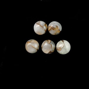 May include: Five round, polished gemstones with a white base and intricate gold-colored veining. The stones are set against a black background, highlighting their natural beauty and unique patterns. These gemstones are ideal for jewelry making.