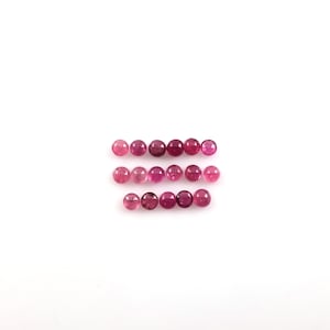 Puede incluir: Una colección de 18 piedras preciosas redondas de color rosa, dispuestas en tres filas de seis. Las piedras preciosas son todas de tamaño aproximadamente igual y tienen un acabado liso y pulido.